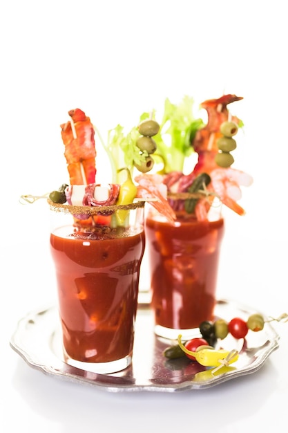 Bloody Mary Cocktail garniert mit Selleriestangen, Oliven und Speckstreifen.