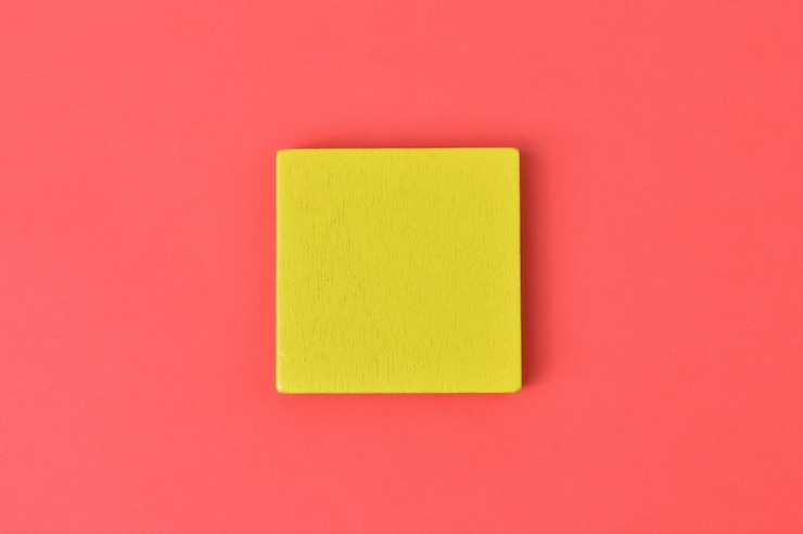 Foto bloque de madera amarillo sobre fondo rojo.