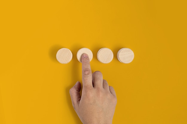 El bloque de madera circular se coloca sobre un fondo amarillo y los gestos de las manos presionan contra el bloque de madera de manera similar a presionar un botón. pancarta con espacio de copia de texto, póster, plantilla de maqueta.