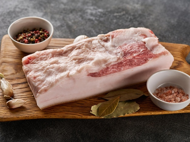 Bloque de panceta de cerdo fresco en tablero de madera con primer plano de sal y pimienta