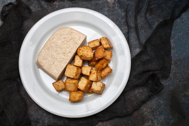 Bloque de tofu crudo en un plato pequeño blanco en la oscuridad