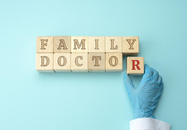 Foto bloques de madera con la inscripción médico de familia y una mano de médico en un guante de látex azul c