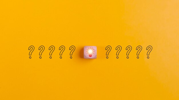 Bloques de madera con signos de interrogación e iconos de bombillas sobre un fondo amarillo para interrumpir las ideas de resolución de problemas y los conceptos de innovación creativa