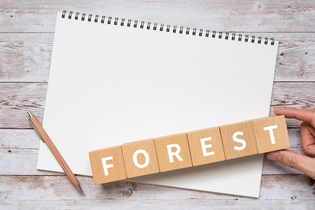 Bloques de madera con el texto del concepto FOREST, un bolígrafo y un cuaderno.