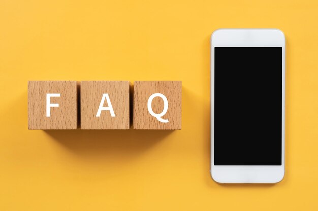 Bloques de madera con texto de concepto de preguntas frecuentes y un teléfono inteligente.