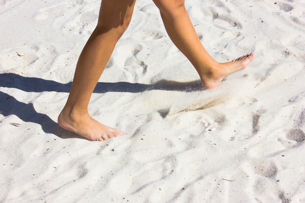 Bloße Füße, die auf den weißen Sand gehen