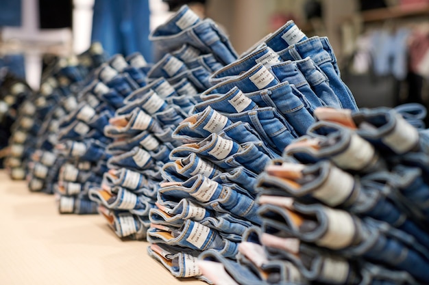 Blue Denim Jeans stapeln sich auf Holztisch oben im Bekleidungsgeschäft im modernen Einkaufszentrum. Gefaltete Baumwolljeans am Schaufenster.