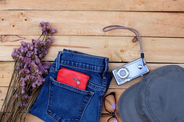 Blue jeans, billetera de cuero rojo, cámara, gafas, flores secas y sombrero sobre fondo de madera