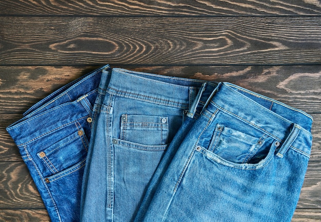 Foto blue jeans en una fila, pila de pantalones de mezclilla, composición en mesa de madera con espacio de copia