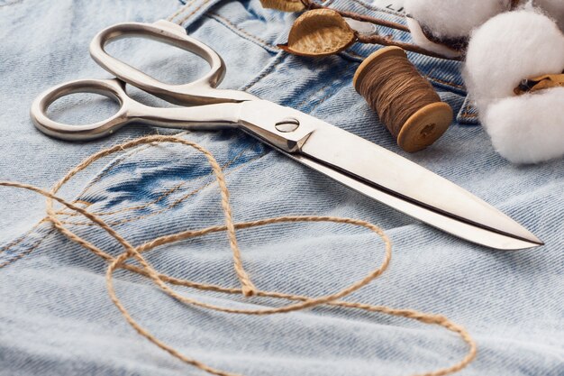 Blue Jeans, Schere, Metallspulen mit Fadennahaufnahme. Schneiderei des lässigen Denim-Bekleidungskonzepts. Schneiden und Nähen, Hintergrund. Natürliche Jeansstoffe.