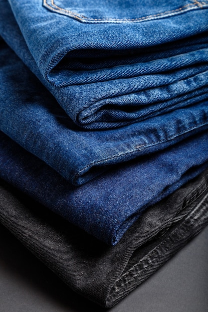 Blue Jeanshosen stapeln Textilbeschaffenheitsgewebehintergrund. Stapel von verschiedenen Blue Jeans, Denim-Jeans-Textilien auf schwarzem Hintergrund.