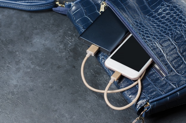 Blue power bank e telefone na bolsa feminina. fundo de concreto cinza escuro. copie o espaço