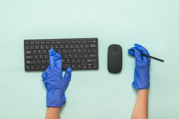 Bluegloved Hände mit einer drahtlosen Tastatur, Maus und Bleistift Prävention der Ausbreitung von Coronavirus