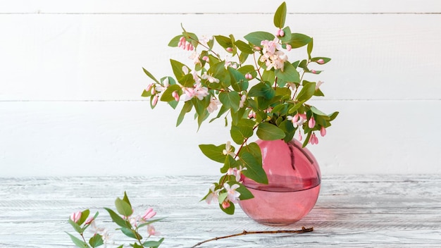 Blühende Frühlingszweige von Blumen in rosa Glasvase auf weißem Holzhintergrund mit Kopierraum Elegantes Zuhause Frühlingsblumendekor Zweig Blumenstrauß Langes Web-Banner