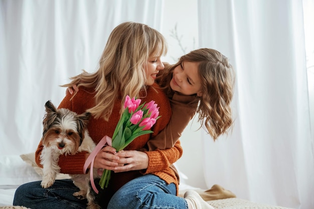 Blumen für den Muttertag halten, sich mit dem Hund umarmen, Eltern mit Tochter zu Hause