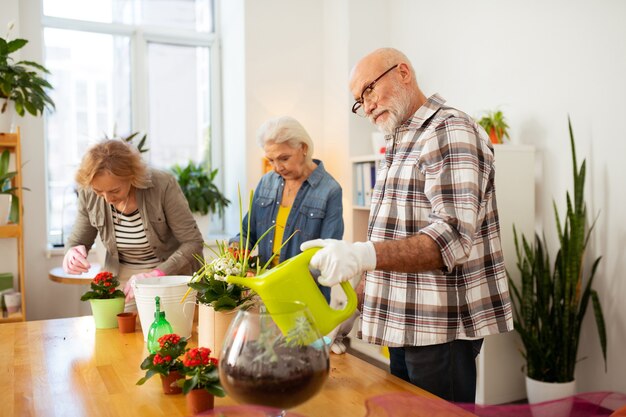 Foto blumen gießen. angenehmer alter mann, der einen bewässerungstopf hält, während er blumen gießt