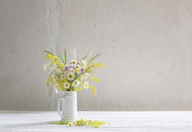 Blumen im weißen Krug auf weißer Wand