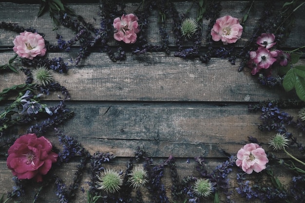 Blumen in einem Kreis auf einem hölzernen Hintergrund Postkarte für den Urlaub Rosen, Geranien, Lavendel, Salbei und behaarte Kastanien werden an den Rändern auf dunklen Brettern platziert