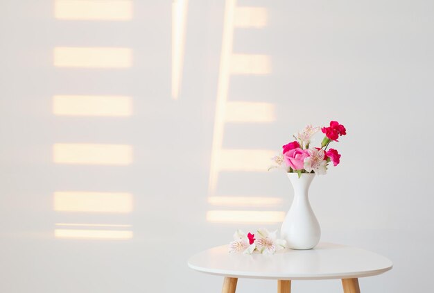 Blumen in weißer Vase auf weißem Hintergrund im Sonnenlicht