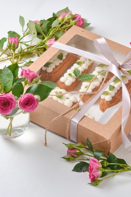 Blumen und eclairs dekoriert mit creme und minze auf einem weißen tisch. dessert für ein romantisches date. kuchen für den urlaub.