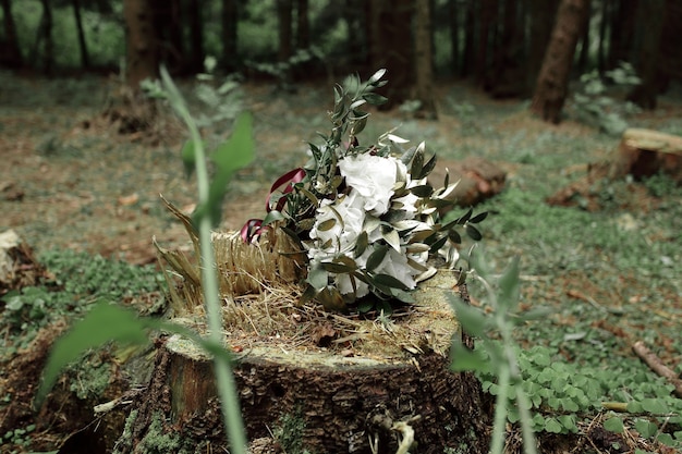 Blumenarrangement auf einem Baumstumpf im Wald.