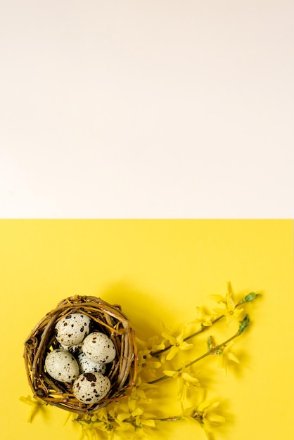 Blumenarrangement Ein blühender Zweig, Eier und Nest auf gelbem, pastellfarbenem Hintergrund Frühling Ostern