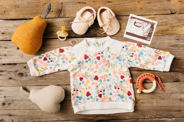 Foto blumenbabykleidung mit schuhen; schnuller; ultraschallbild und stofftier auf holztisch