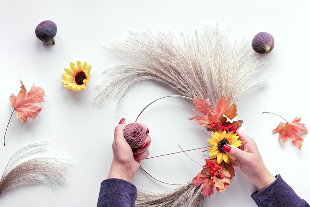 Blumenkranz aus trockenem Pampasgras und Herbstlaub Hände binden Dekorationen an Metallrahmen