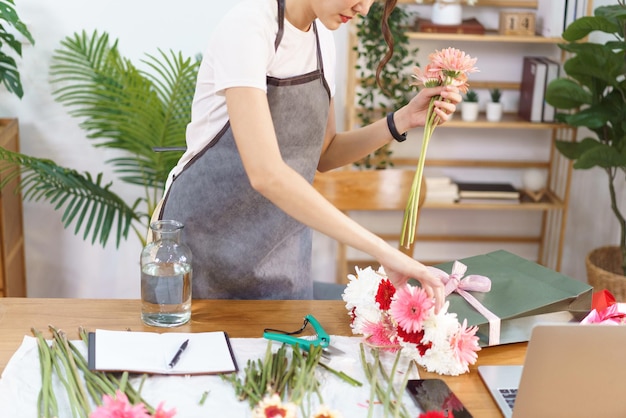 Blumenladenkonzept Weibliche Floristin greift nach bunten Gerbera in der Einkaufstasche, um sie in der Vase zu arrangieren