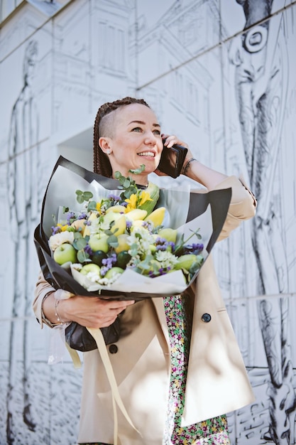 Blumenlieferung Junge, moderne Hipster-Frau mit Handy, die einen schönen Blumenstrauß von empfängt