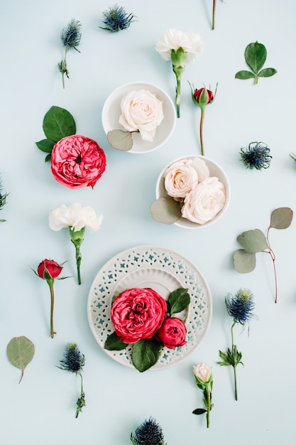 Blumenmuster aus roten und beige Rosen auf Teller, weißen Nelken und Eukalyptuszweigen auf blassem pastellblauem Hintergrund. Flache Lage, Ansicht von oben