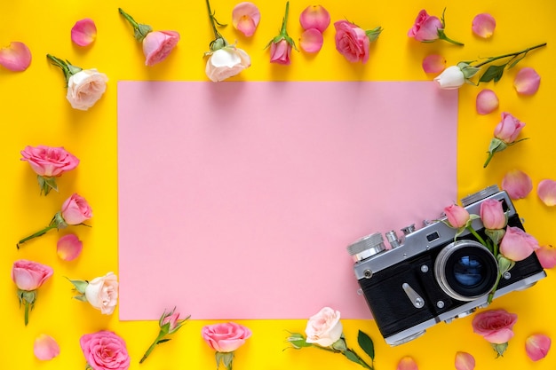 Blumenmuster des runden Rahmens gemacht von den rosa und beige Rosen, von den Grünblättern und von der Filmkamera auf gelbem Hintergrund Valentinstaghintergrund.