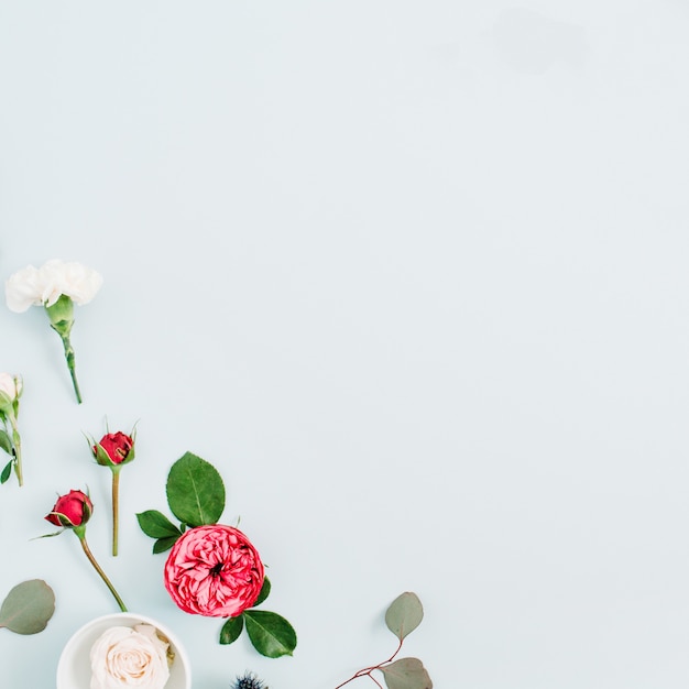 Blumenrahmen aus roten und beigen Rosen, weißen Nelken und Eukalyptuszweigen auf blassem pastellblauem Hintergrund. Flache Lage, Ansicht von oben