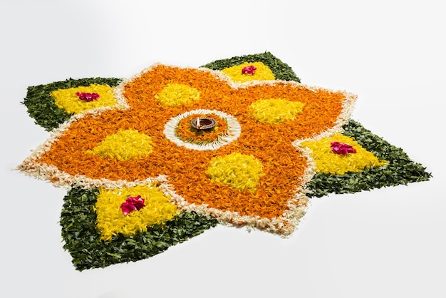 Foto blumenrangoli für diwali oder pongal aus ringelblumen- oder zendublumen und roten rosenblättern auf weißem hintergrund mit tonöllampe in der mitte, selektiver fokus