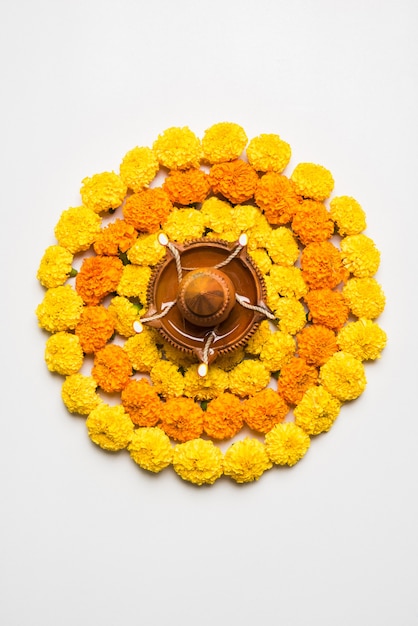 Blumenrangoli für Diwali oder Pongal aus Ringelblumen- oder Zendublumen und roten Rosenblättern auf weißem Hintergrund mit Tonöllampe in der Mitte, selektiver Fokus