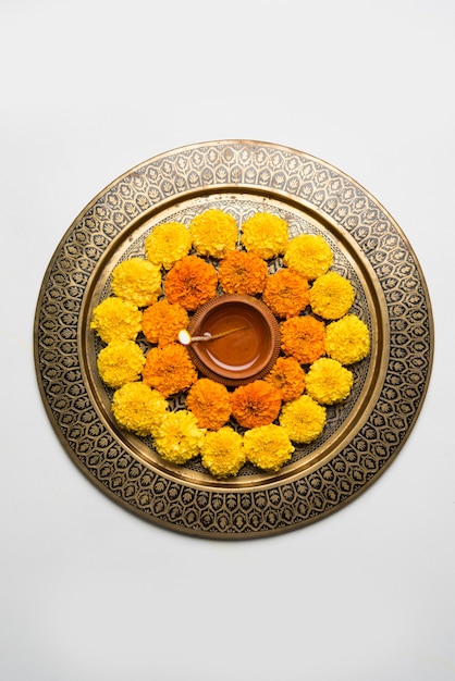 Blumenrangoli für Diwali oder Pongal aus Ringelblumen- oder Zendublumen und roten Rosenblättern auf weißem Hintergrund mit Tonöllampe in der Mitte, selektiver Fokus