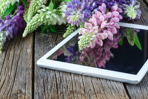 Blumenstrauß auf einem Holztisch mit einem Tablet-Computer