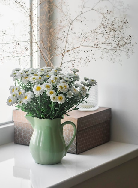 Blumenstrauß aus Chrysanthemen in einem Vintage-Keramikbecher eine Bastelbox auf der Fensterbank Gemütliches Wohnambiente