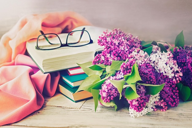 Blumenstrauß aus Flieder, Brille und Büchern auf Holzgrund, getönt.