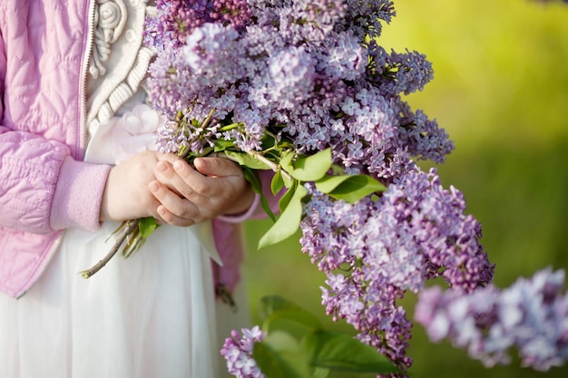 Blumenstrauß aus fliederfarbenen Frühlingsblumen in jungen Mädchenhänden auf grünem Hintergrund Nahaufnahmebild