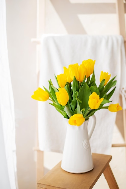 Blumenstrauß aus gelben Tulpen in einer weißen Keramikvase auf dem Hintergrund des Fensters Sonniges Foto