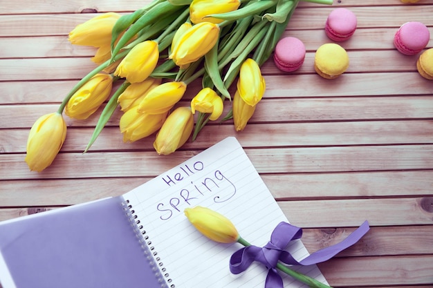 Blumenstrauß aus gelben Tulpen mit der Aufschrift "Hallo Frühling" auf Holzhintergrund