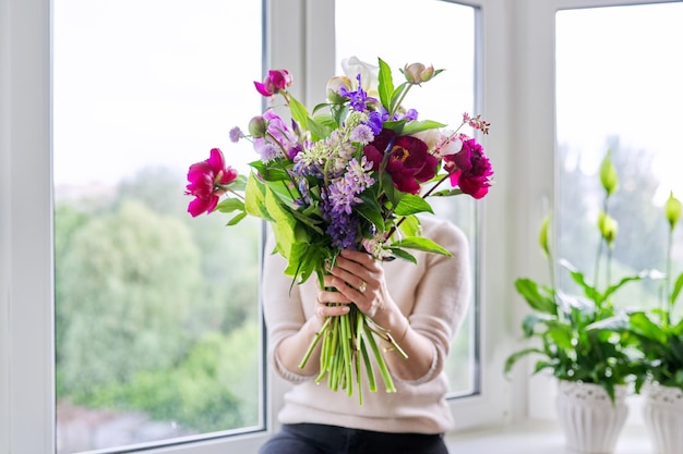 Blumenstrauß aus hellen Blumen von Pfingstrosen Iris Lupinen in den Händen der Frau in der Nähe