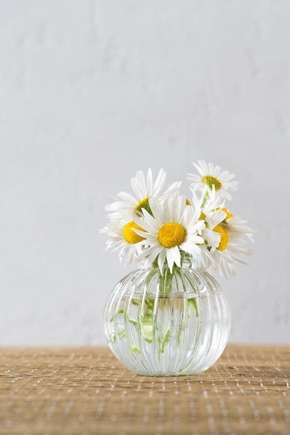 Blumenstrauß aus Kamillenblüten in Glasvase auf einer Weidenmatte Vertikale Nahaufnahme