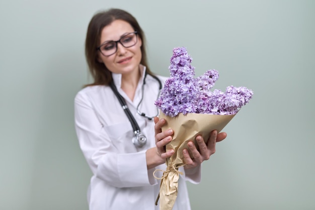 Blumenstrauß aus lila Blumen in den Händen der Ärztin mit Stethoskop. Weltgesundheitstag, glückliche Krankenschwester mit Blumen auf grünem Hintergrund