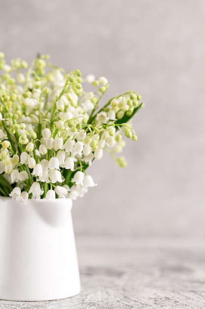 Blumenstrauß aus Maiglöckchen in einem weißen Glas auf grauem Betongrund.