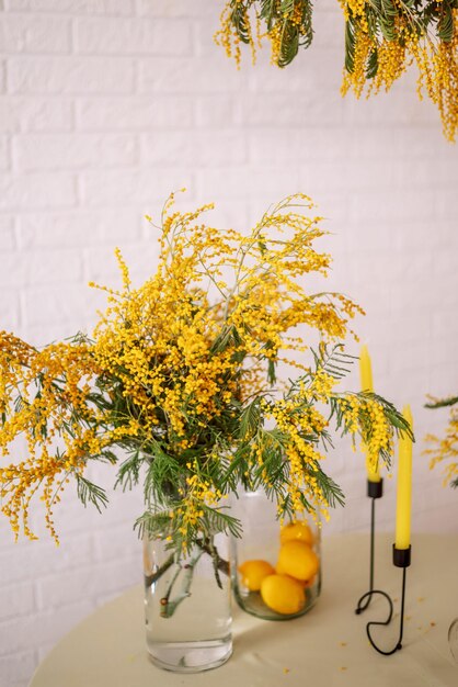 Blumenstrauß aus Mimosen auf dem Tisch in einer Glasvase Osterdekor und Zitronen