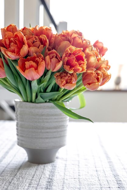 Blumenstrauß aus orangefarbenen Tulpen in einer Vase auf einem verschwommenen hellen Hintergrund
