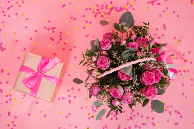 Blumenstrauß aus rosa Rosen in einem Weidenkorb und einer Geschenkbox mit einer Schleife auf einem rosa Tischhintergrund Geburtstag Hochzeit Muttertag Valentinstag Frauentag Draufsicht