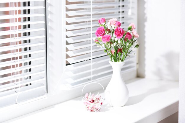 Blumenstrauß aus rosa Rosen in weißer Vase auf Fensterbankhintergrund